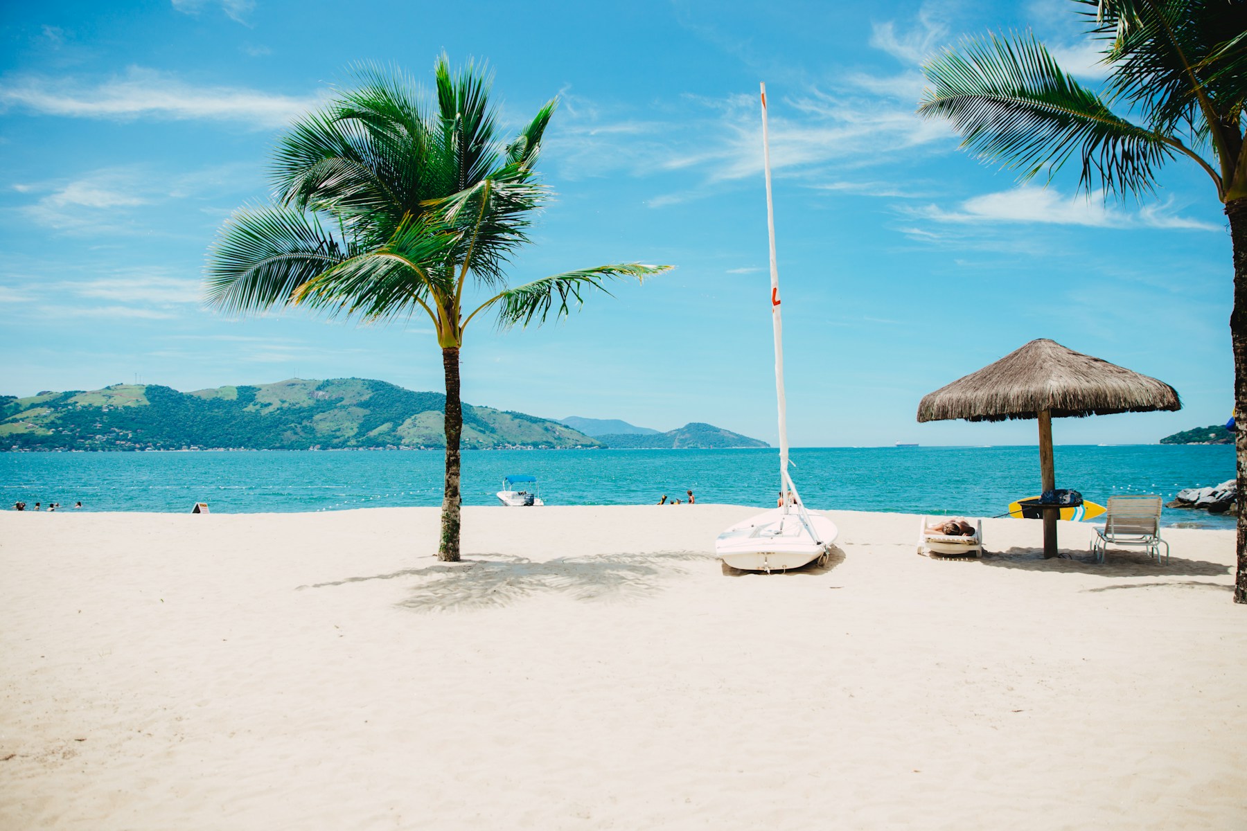 A palm-fringed beach with turquoise water and a sun lounger